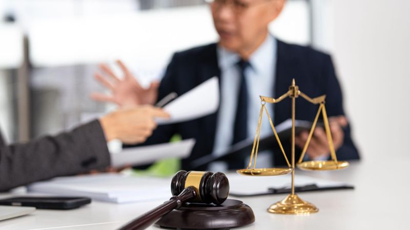 Gavel and scales on desk during legal discussion between professionals at a law office.