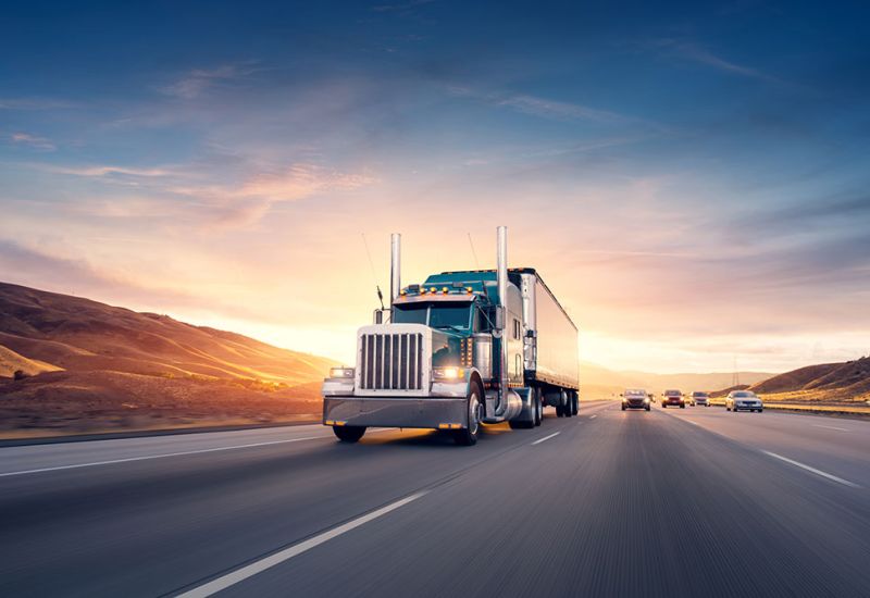 Powerful semi-truck driving on highway at sunset, with scenic mountains in the background.