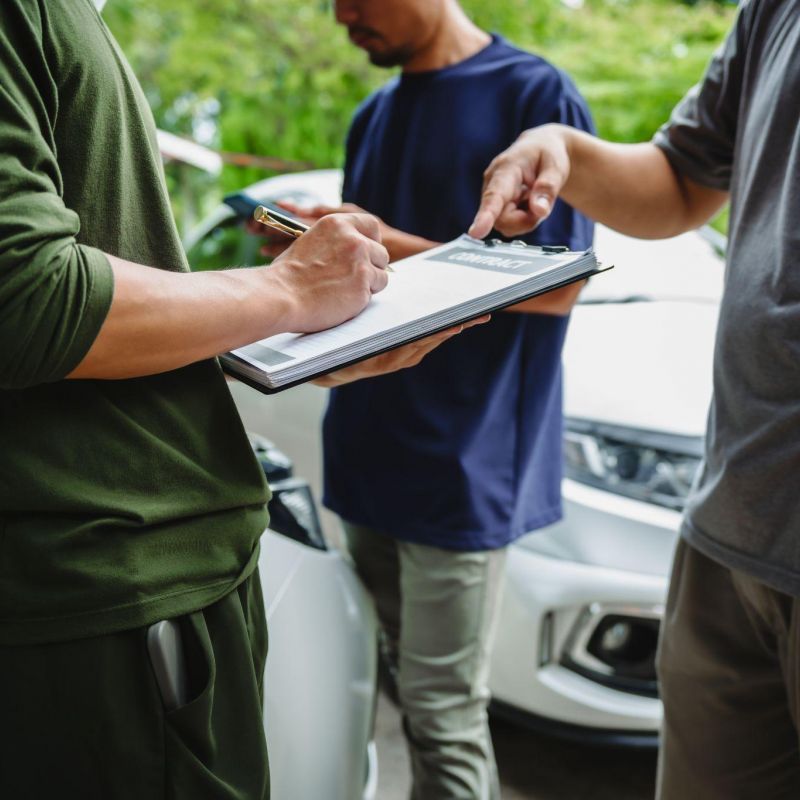 People signing a contract near a car, emphasizing agreement and negotiation dynamics in an outdoor setting.