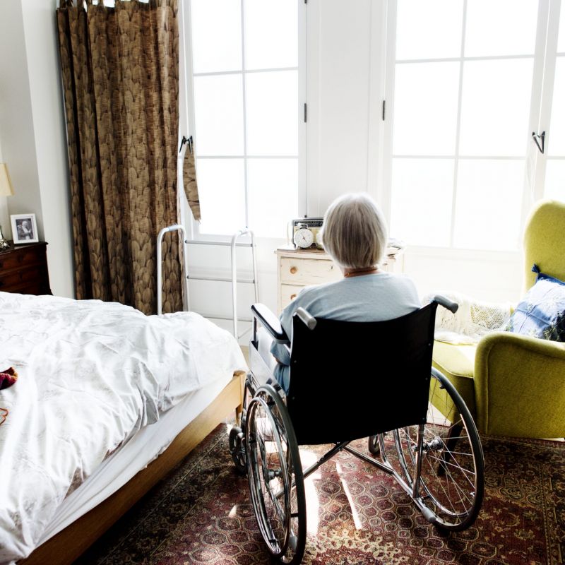 Elderly woman in a wheelchair sitting in a cozy bedroom, symbolizing the importance of accessibility and comfortable living environments.