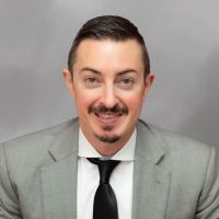 Andrew M. Coffarelli in a suit with shoulder-length hair and a patterned tie, smiling in a portrait