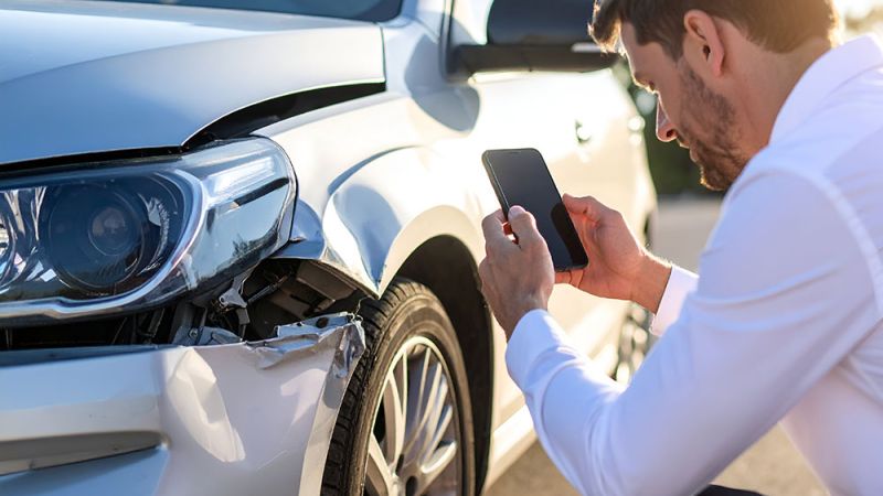 Man photographing car accident damage for insurance claim documentation.