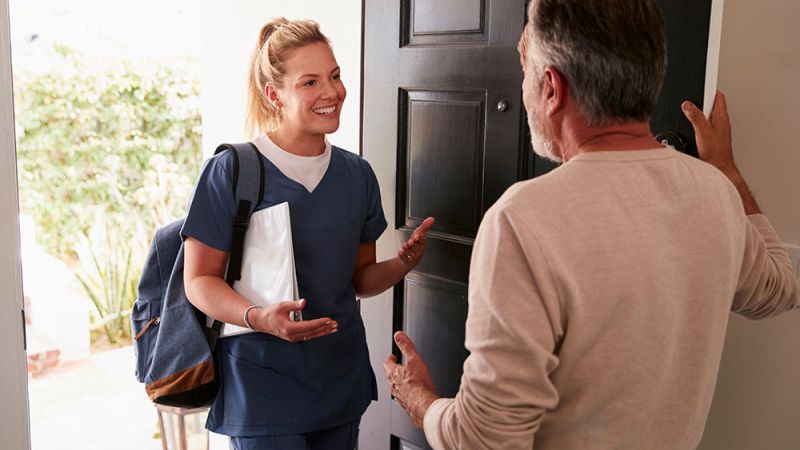 Healthcare professional greeting a senior man at home, providing in-home care services.