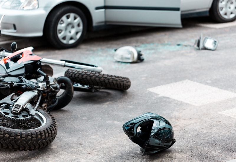 Motorcycle accident scene with a helmet on the road, near a car with damage.