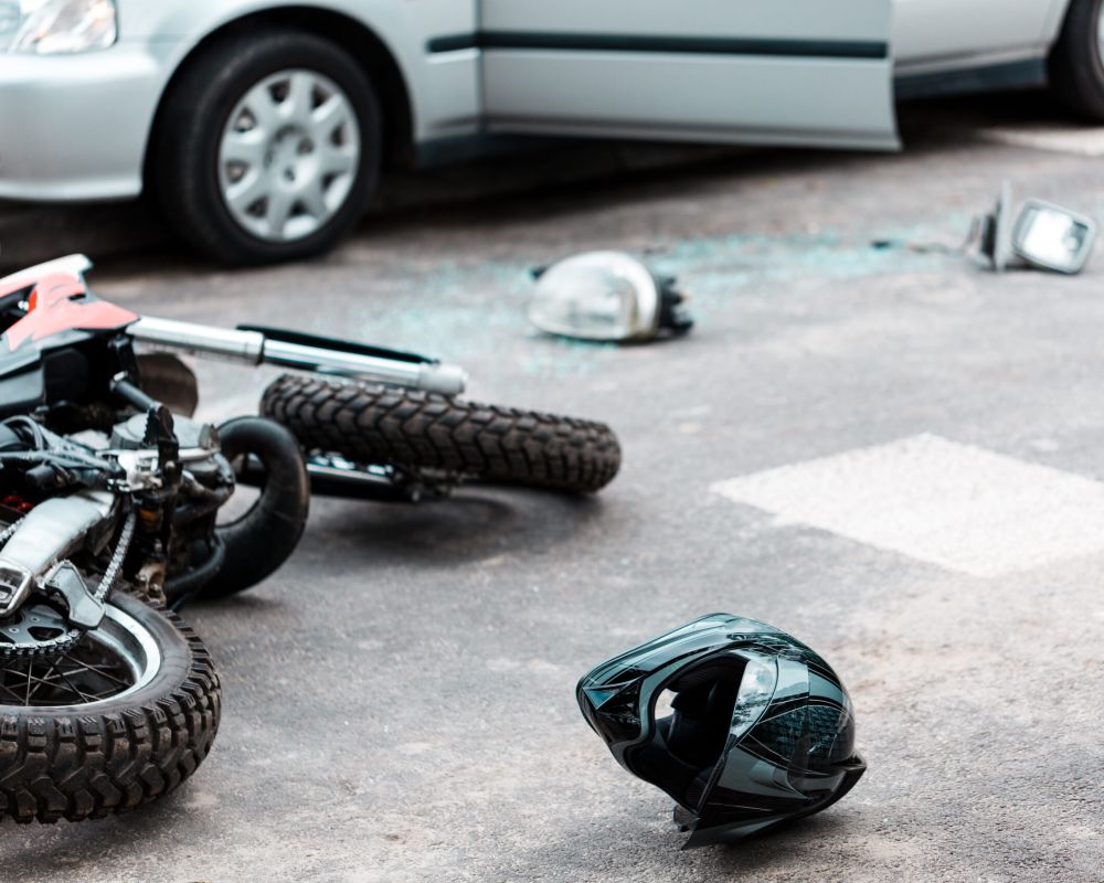 Motorcycle accident scene with a helmet on the road, near a car with damage.