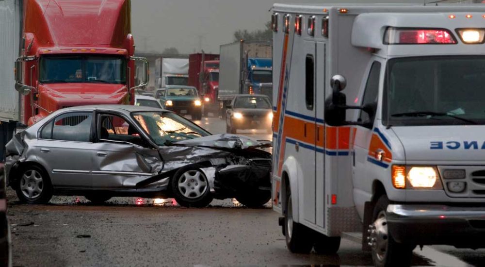 Multivehicle accident involving car and truck with ambulance on rainy highway. Emergency response on scene.