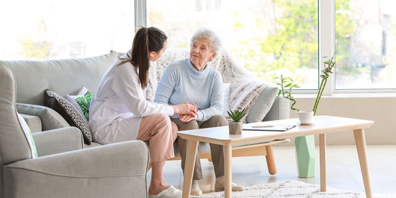 Caregiver and elderly woman sitting in a cozy living room, having a supportive conversation.