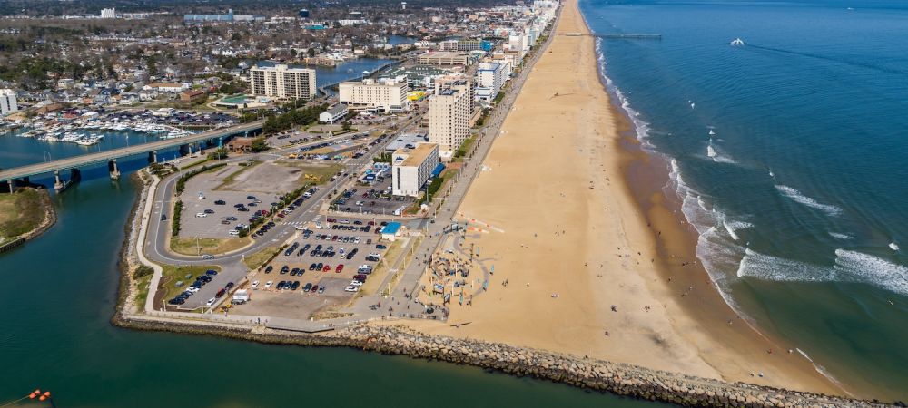 Aerial view of Virginia Beach oceanfront, showing sandy beach, ocean waves, and hotels lining the shore.
