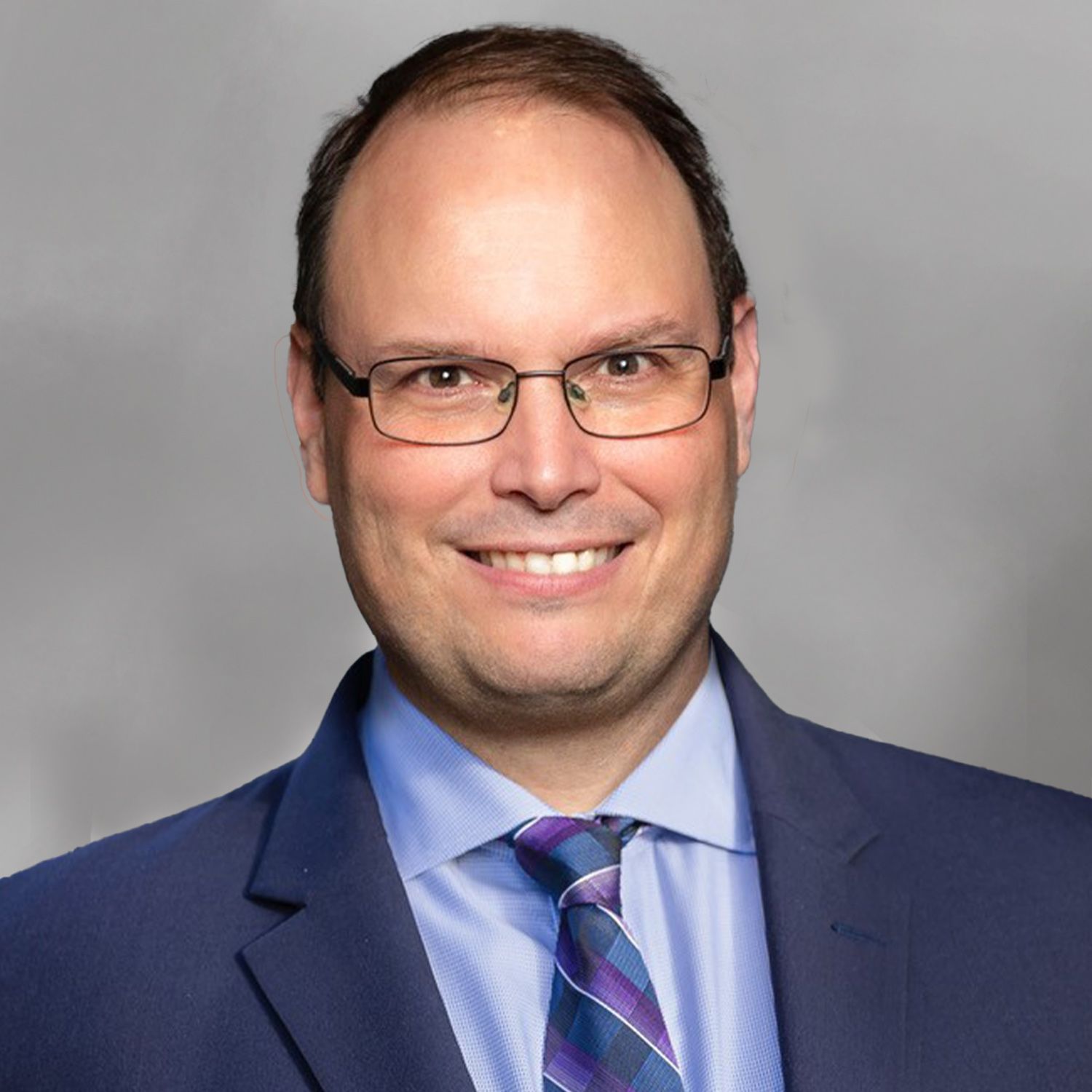 Joseph T. Musso in a suit with shoulder-length hair and a patterned tie, smiling in a portrait