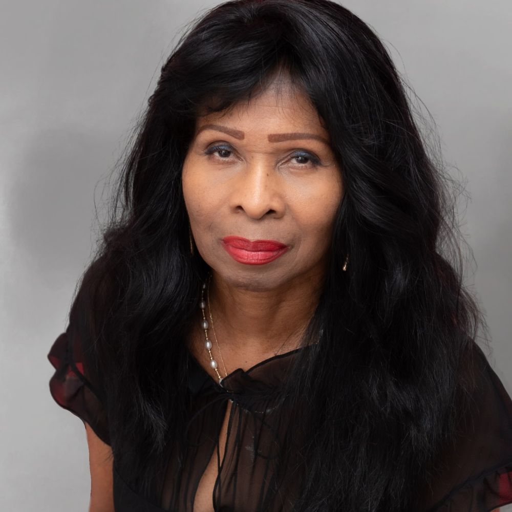 Wanda Smith with long black hair and red lipstick, wearing a black blouse, against a gray background.