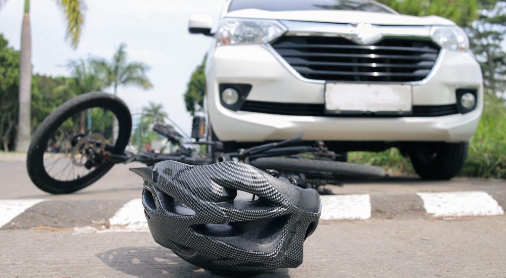 Bicycle accident scene with helmet on road near white car and a fallen bike, highlighting road safety.