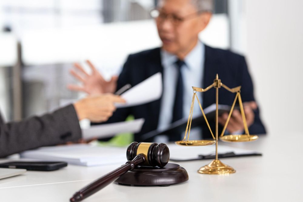 Gavel and scales on desk during legal discussion between professionals at a law office.
