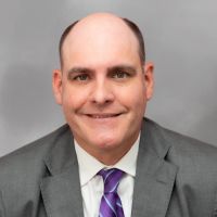 T. Wayne Williams in a suit with shoulder-length hair and a patterned tie, smiling in a portrait
