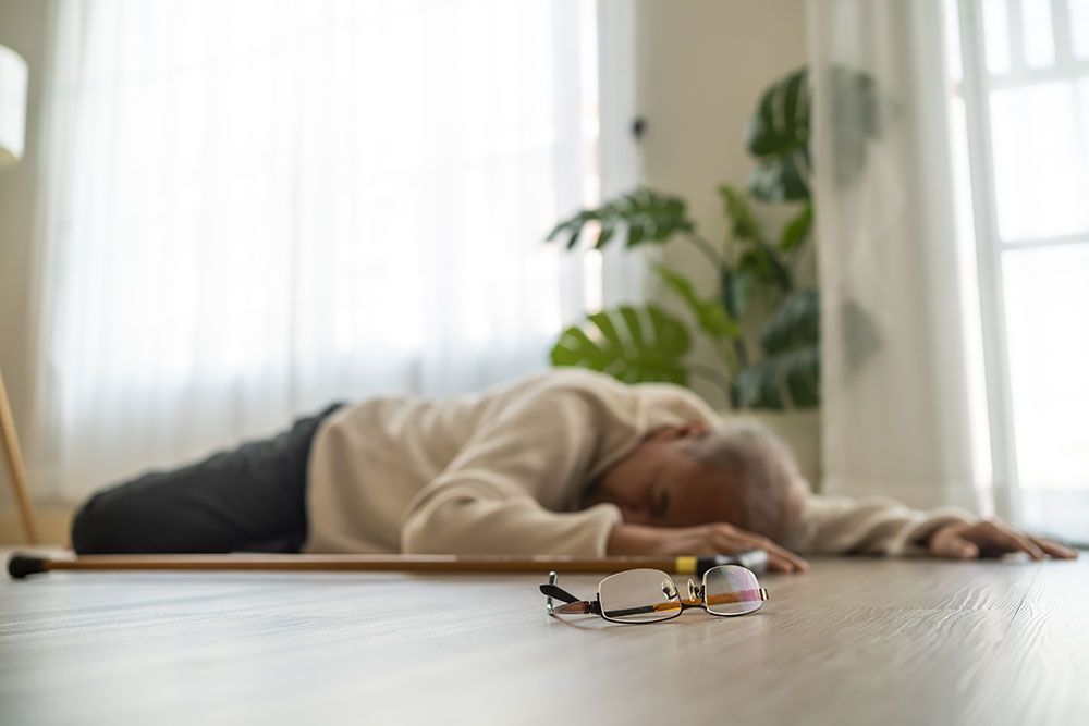 Elderly person fallen on floor with walking stick and glasses nearby, implying medical emergency or fall risk.