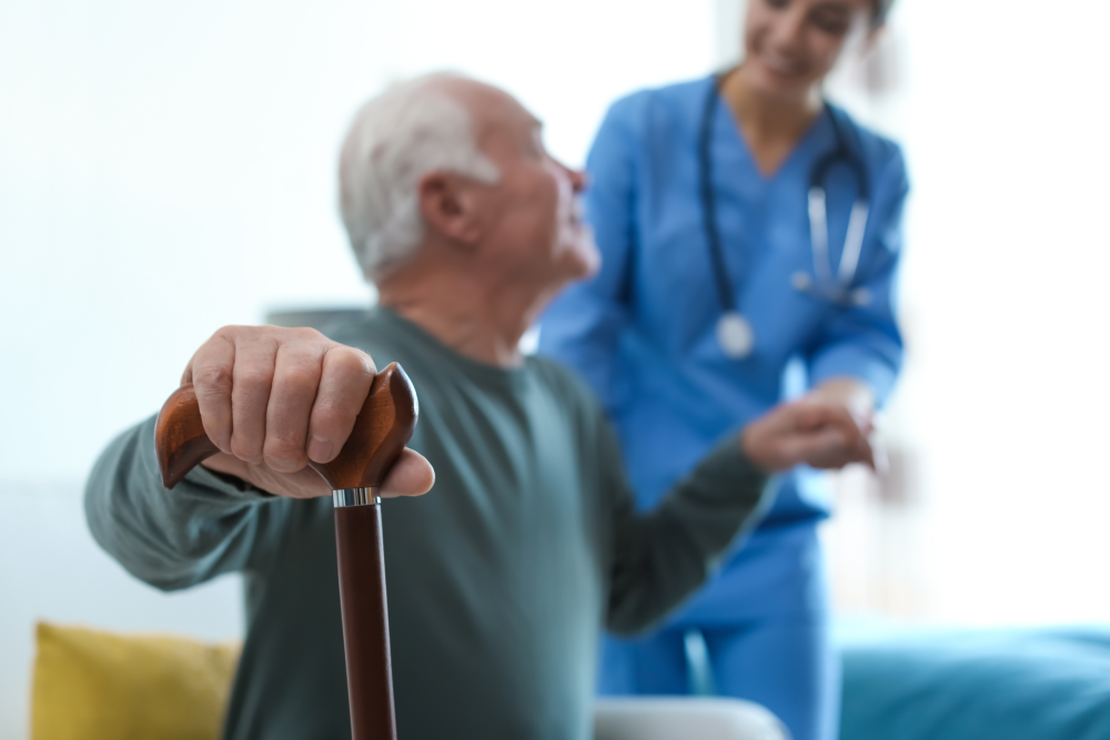 Senior man with cane and nurse in blue uniform indoors.