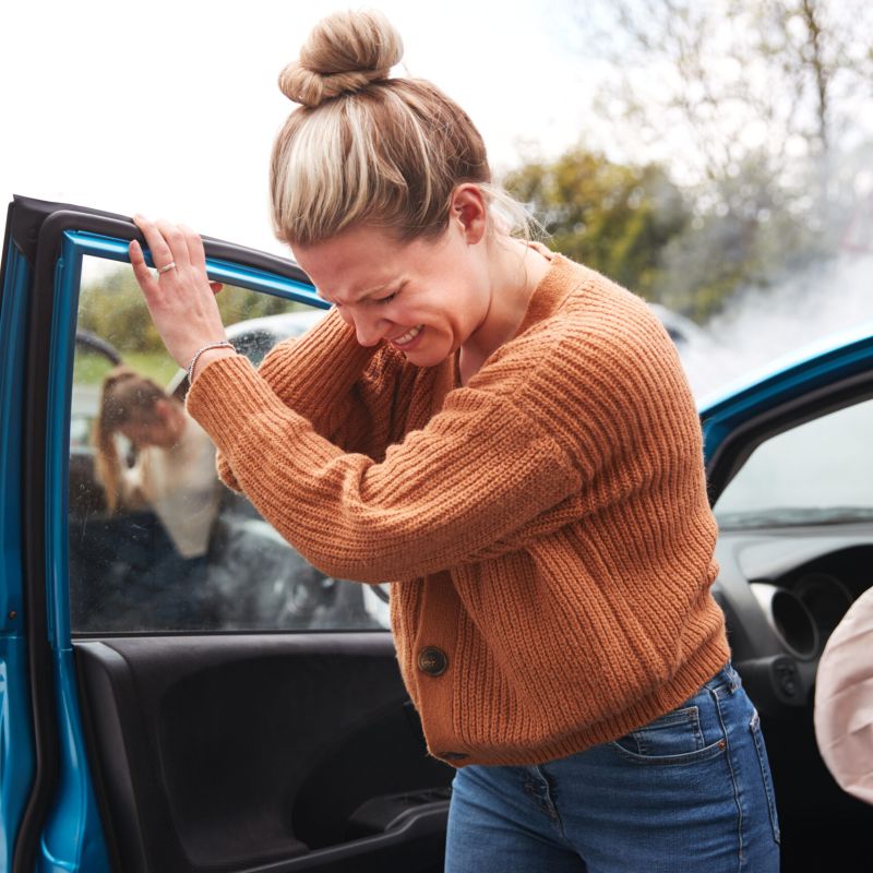 Grupo de personas de pie cerca de coches dañados por la noche, con bengalas de emergencia rojas y humo, ilustrando las consecuencias de un accidente automovilístico.