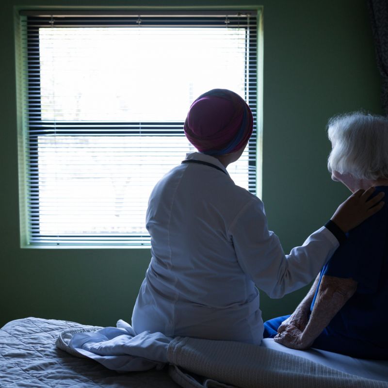 Nurse comforting an elderly woman by a window, symbolizing support and the importance of knowledge in nursing home advocacy.