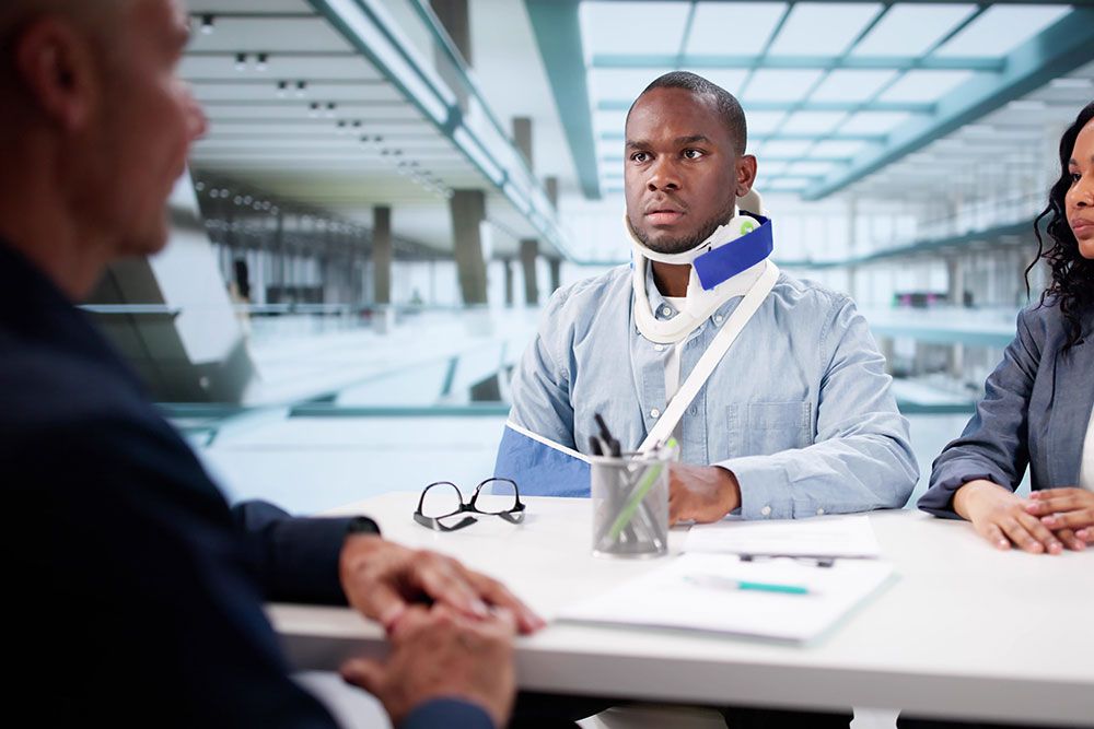 Man with neck brace and arm sling discussing with professionals in office setting.
