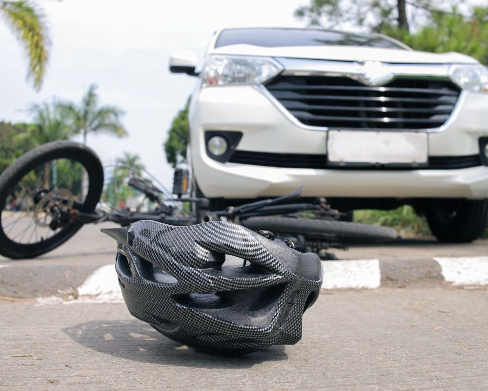 Bicycle accident scene with helmet on road near white car and a fallen bike, highlighting road safety.