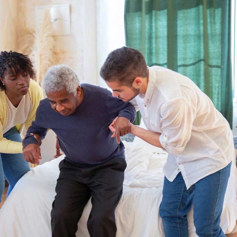 Female and male nursing home attendants helping an elderly man stand up