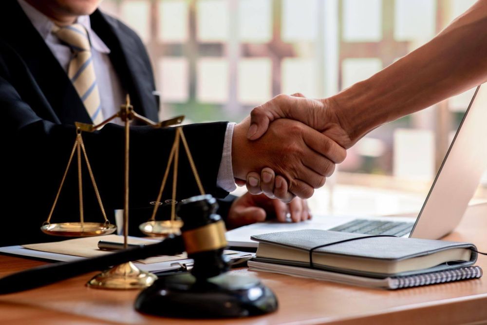 Handshake between lawyer and client at office desk with legal documents.