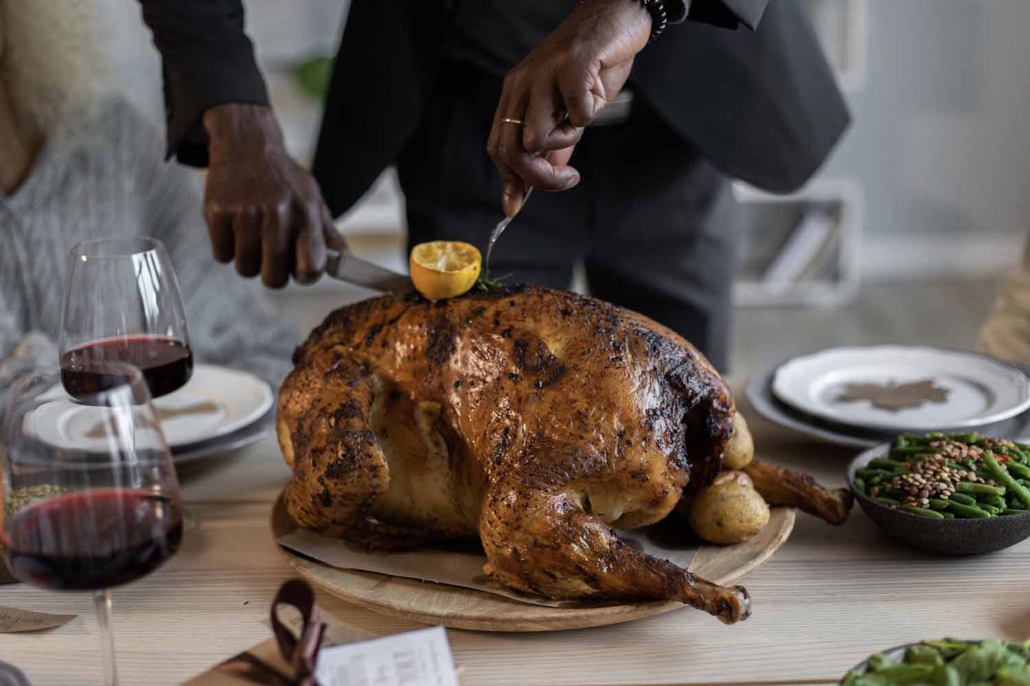 Man carving a deep fried turkey next to two glasses of red wine and a side of green beans for Thanksgiving dinner