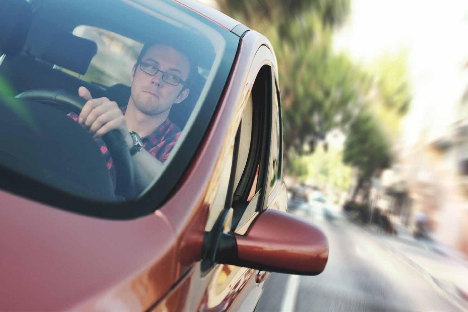 Man wearing glasses driving a red car
