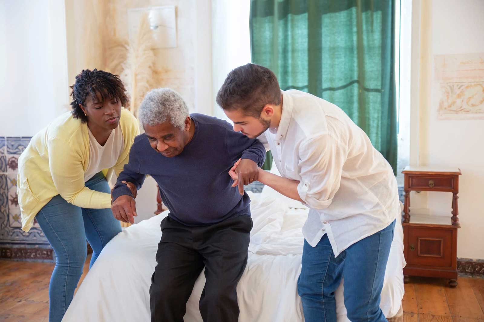 Female and male nursing home attendants helping an elderly man stand up