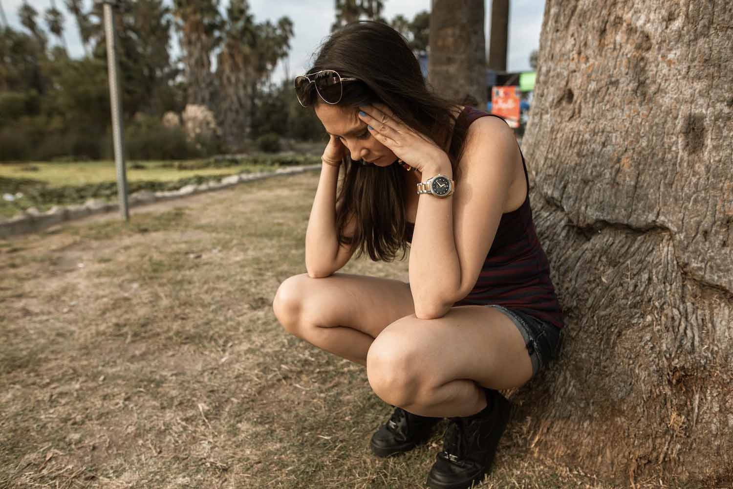 Woman crouches near a tree, stressed after a hit and run