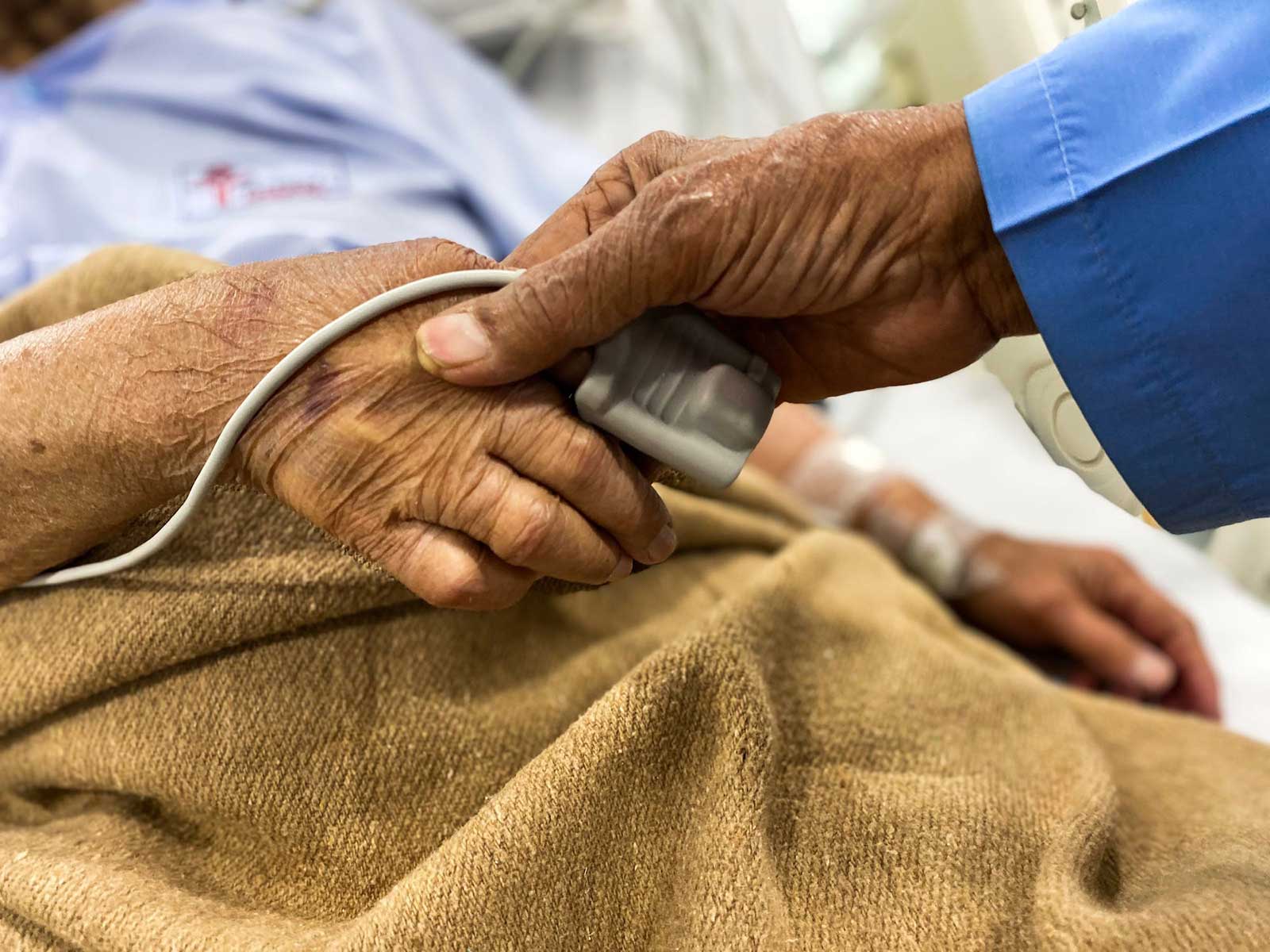 Elderly hand with a pulse oximeter being held by another hand, in a nursing home