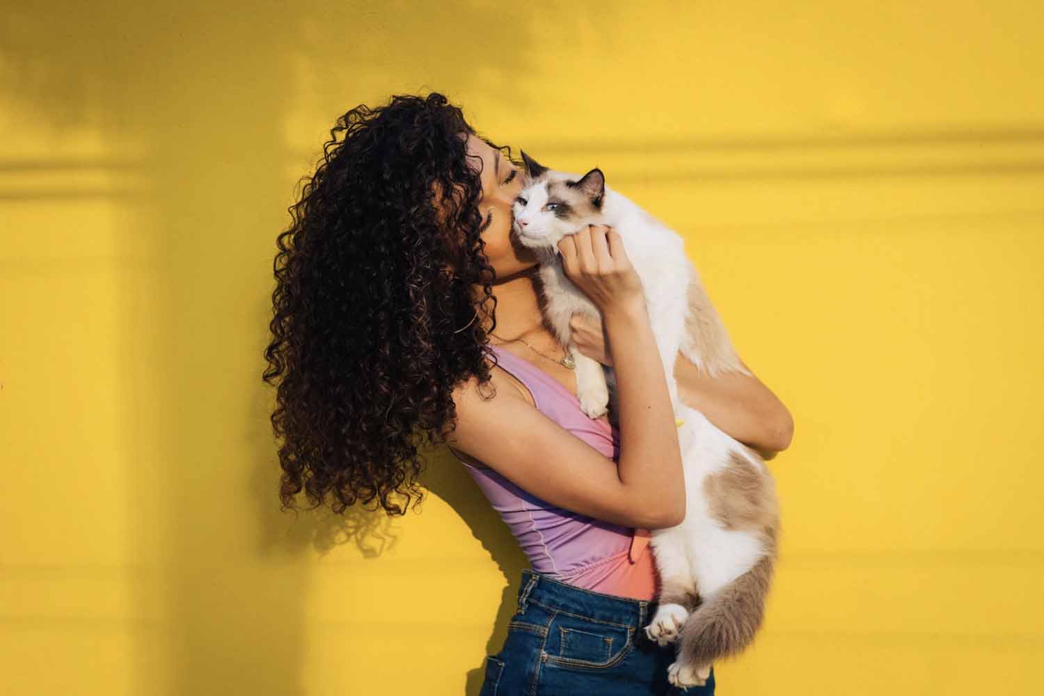 Woman hugging a brown and white cat in front of a yellow wall