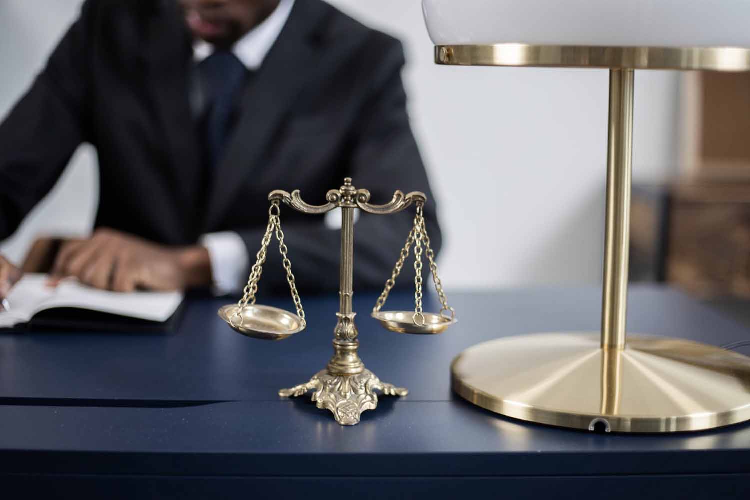 The scales of justice sitting on an attorney’s desk, next to a lamp