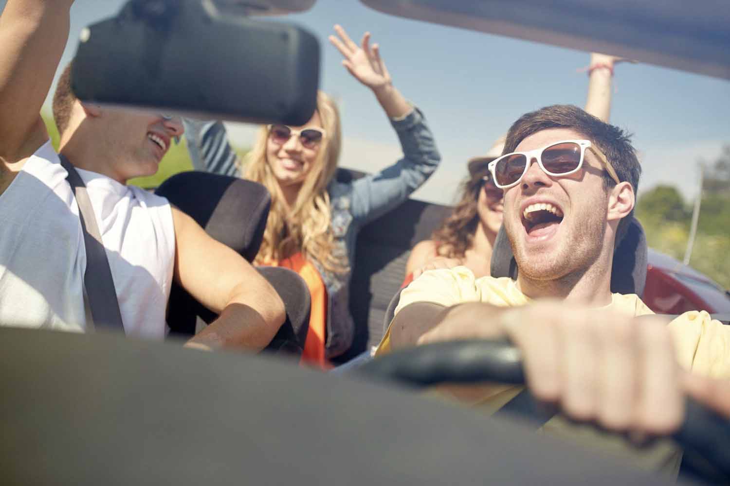 Four teens driving in a convertible having fun, but being very distracting to the young driver