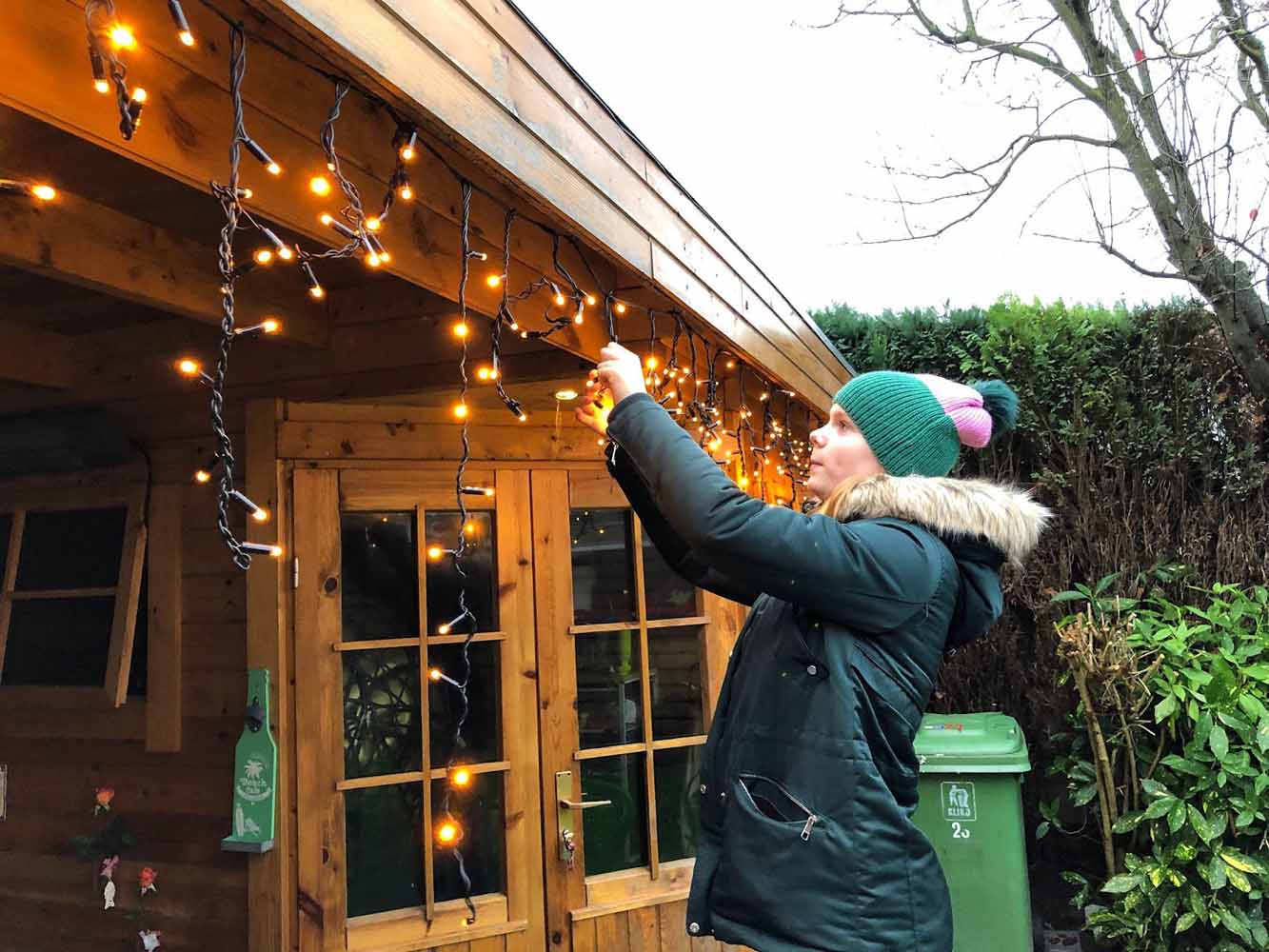 Girl hanging outdoor holiday lighting, practicing safe decorating habits by using outdoor rated lighting and equipment.