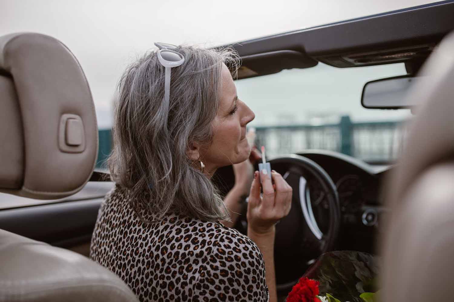 Older woman in driver seat practicing unsafe driving behavior by applying makeup and taking eyes off of the road to look in the mirror.