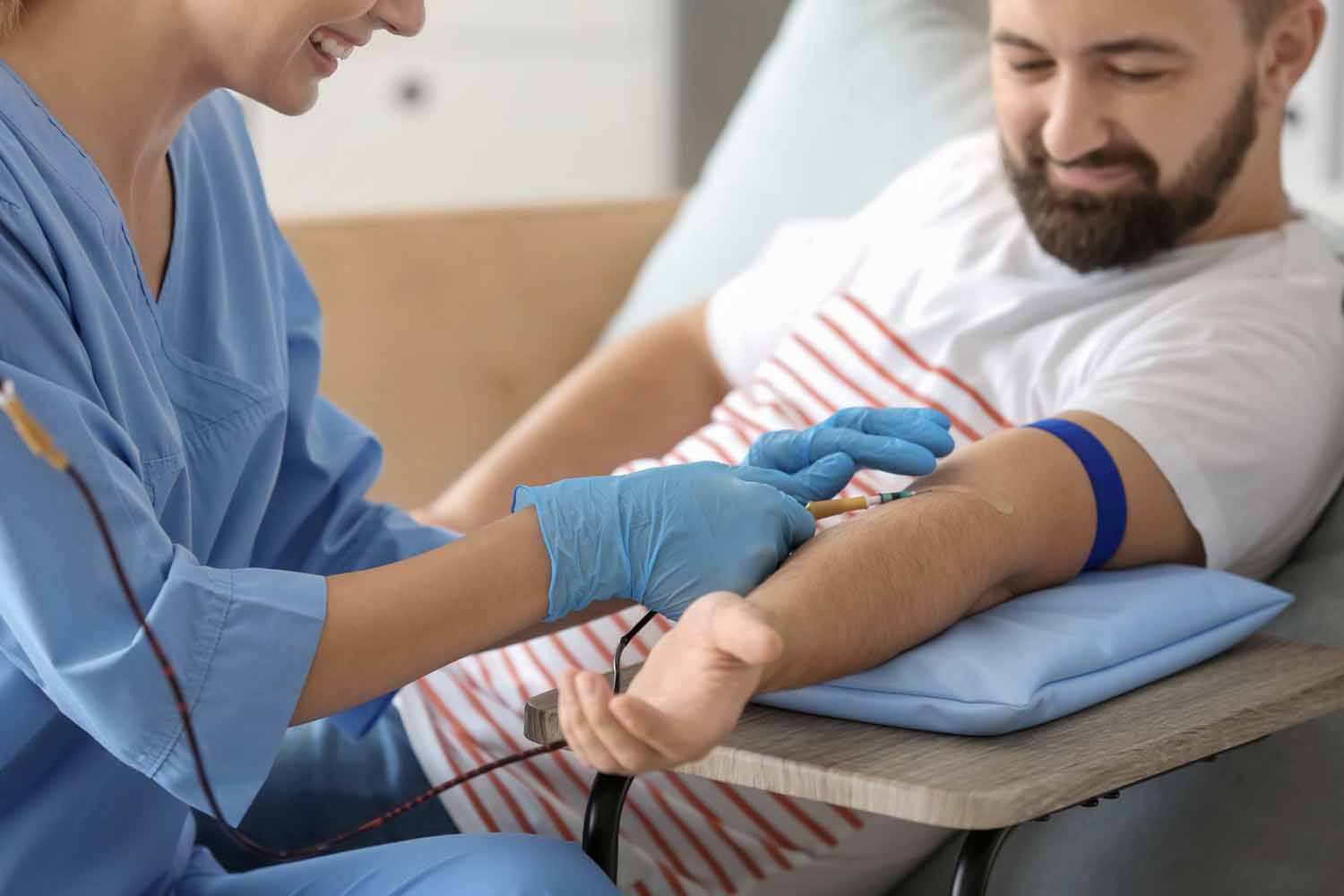 Woman inserting a blood collection needle into a man’s arm