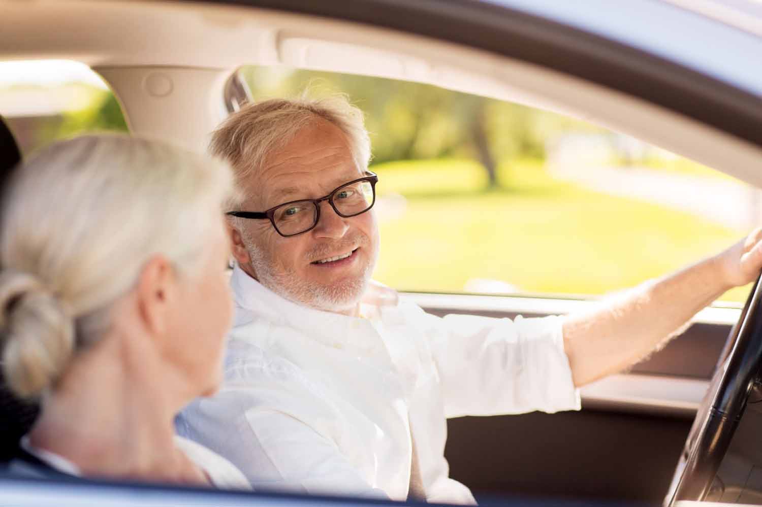 Older senior couple smiling and happy driving in the car. Husband is driving the wife in daylight, practicing safer driving habits.