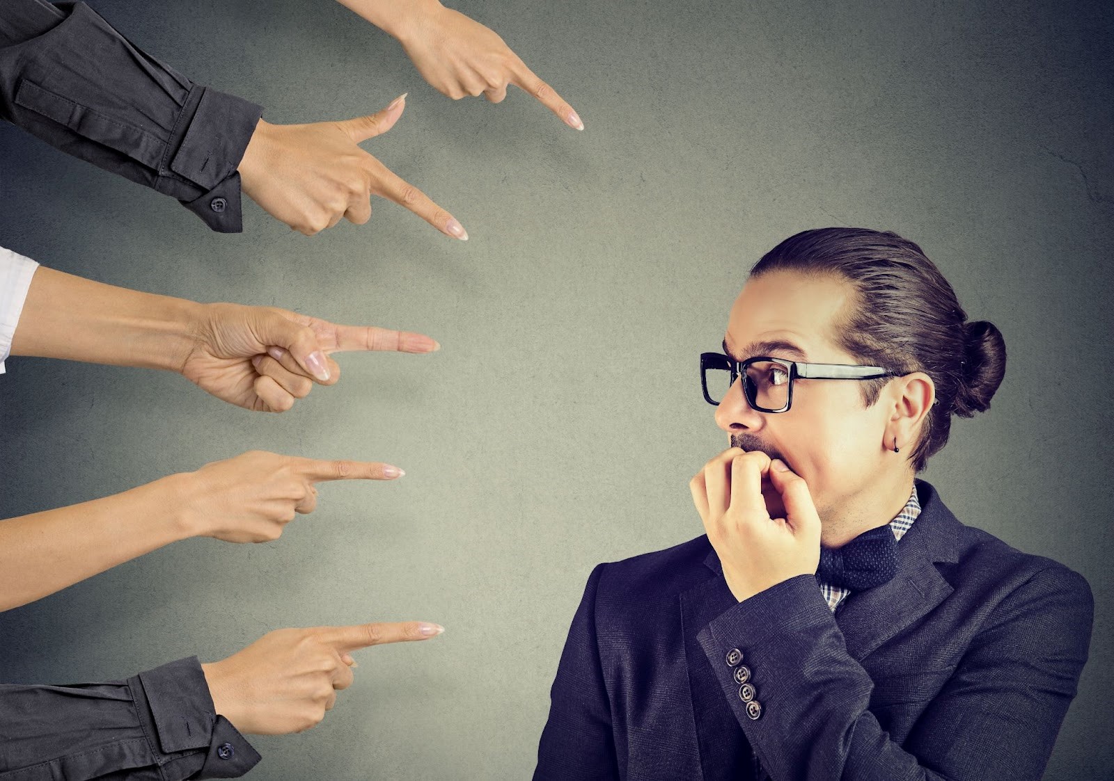 Anxious, guilty man being judged by multiple people all pointing at him