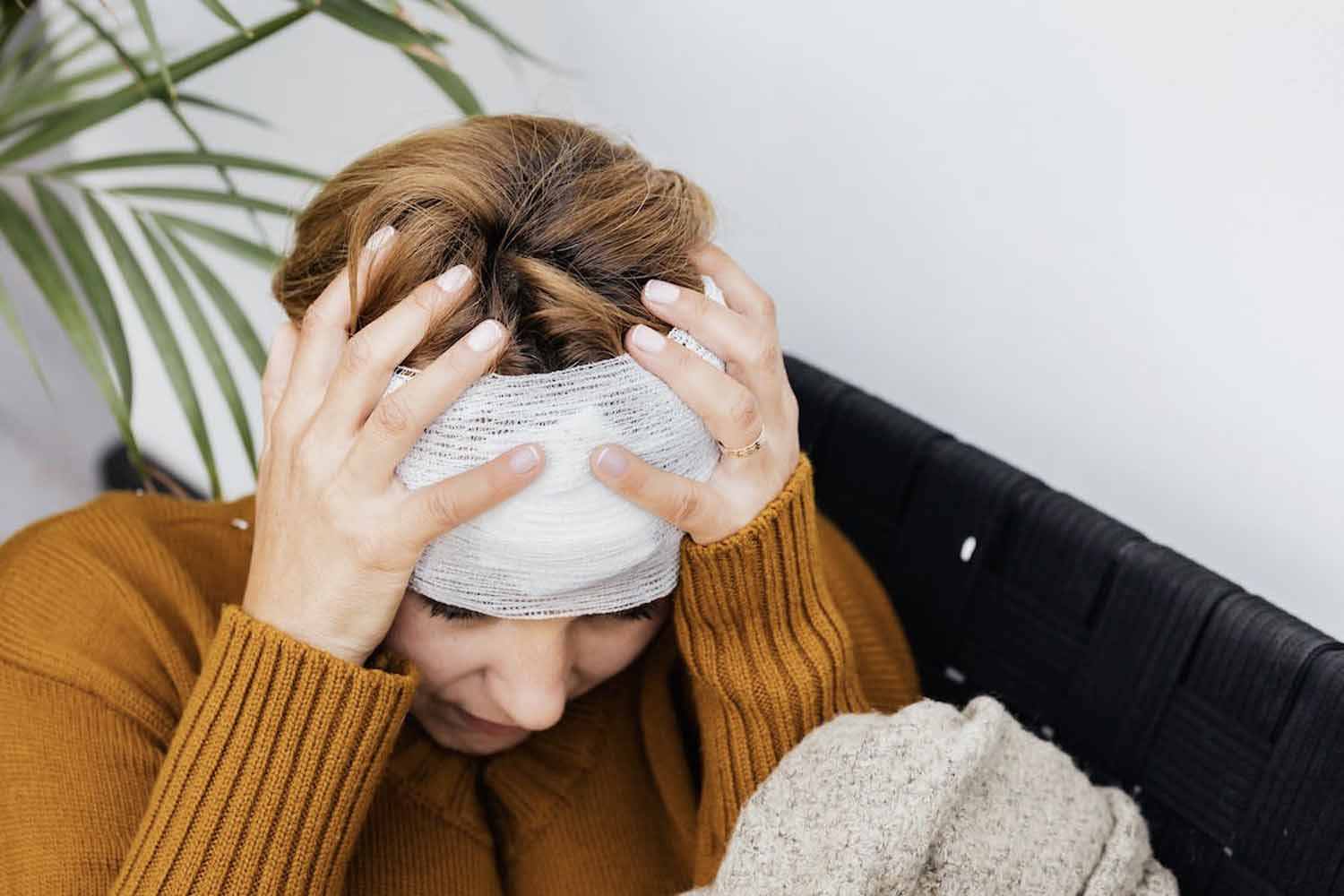 Woman holds her head that’s wrapped up in a bandage