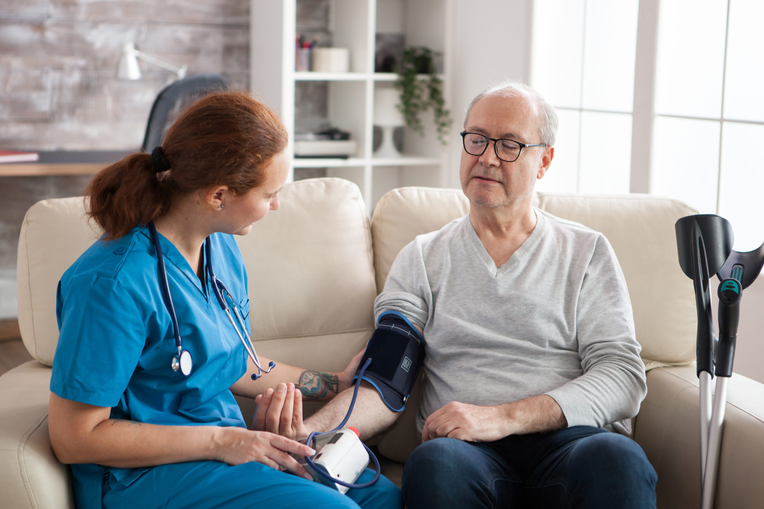 Senior man in nursing home with digital blood pressure device on his arm with female nursing assistant.