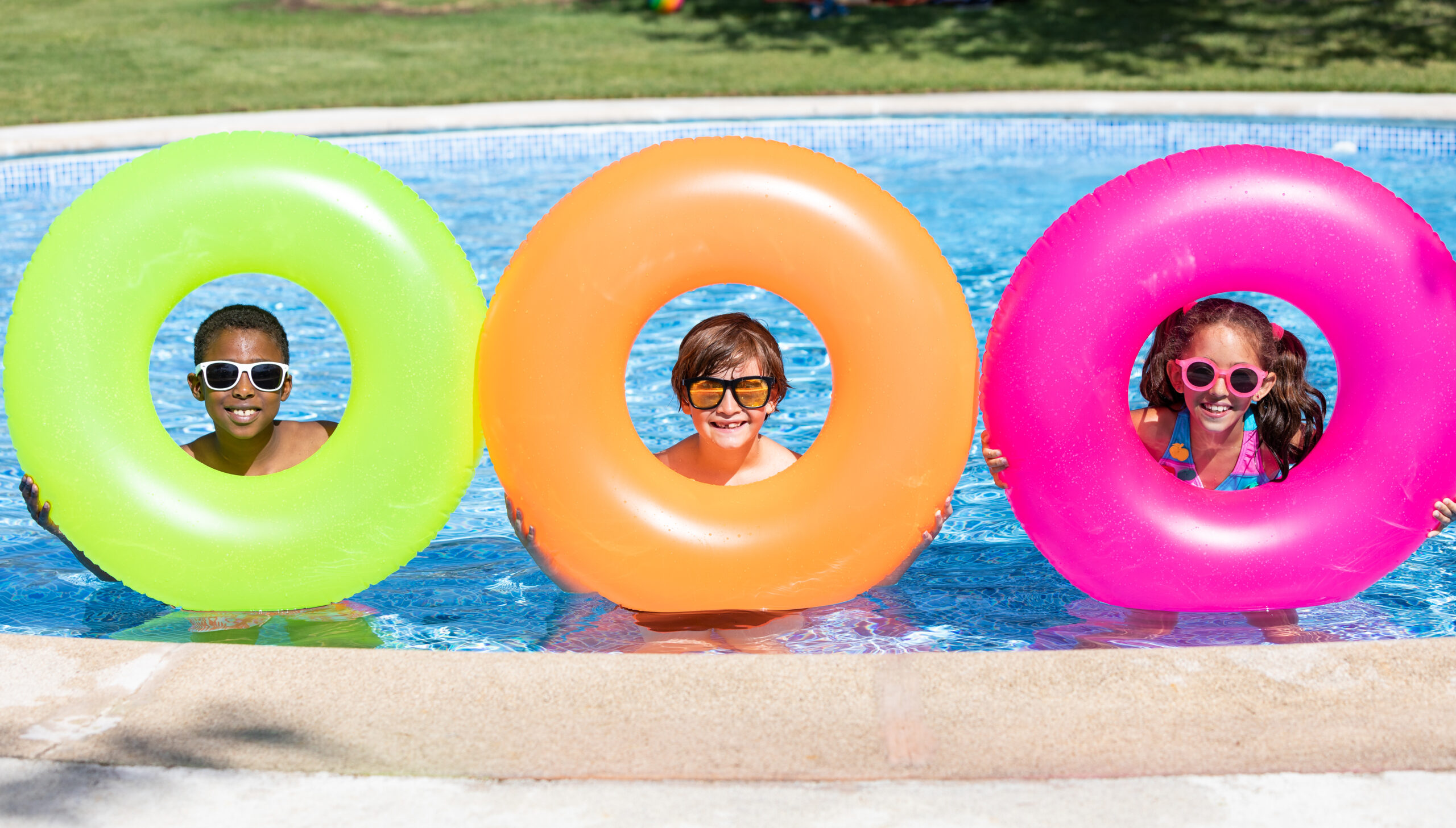 kids smiling and happy at the pool holding up colorful innertubes