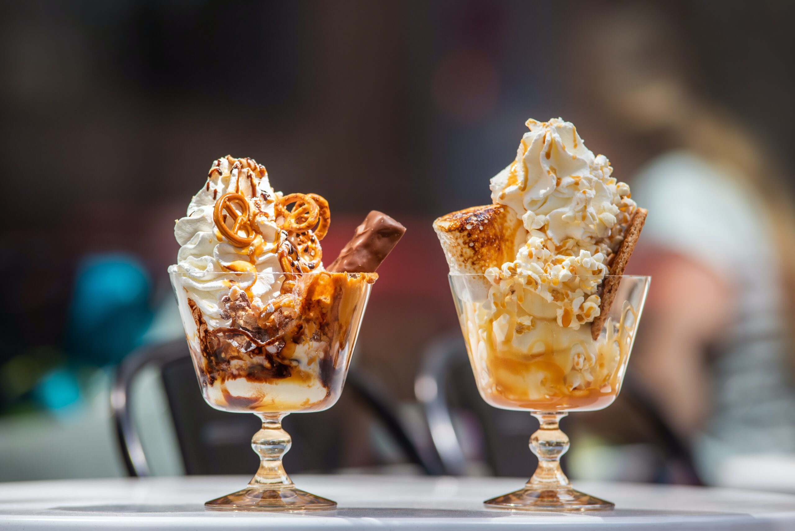 2 ice cream sundaes with pretzels, candy bars, toasted marshmallows, graham crackers, chocolate and caramel sauces drizzled on top.