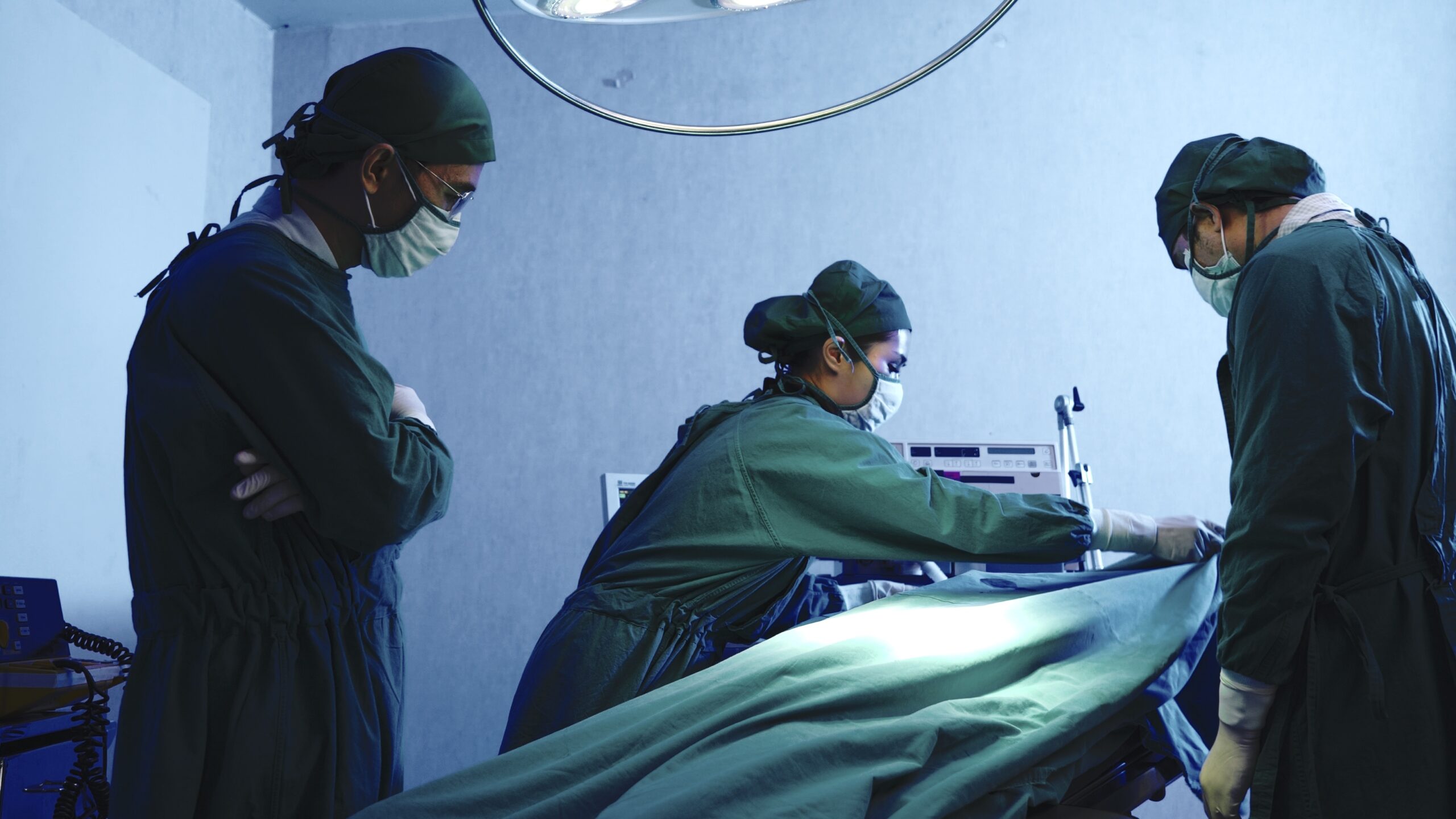 Surgeon covering a patient that died during surgery with a sheet. Two other doctors look on, sad
