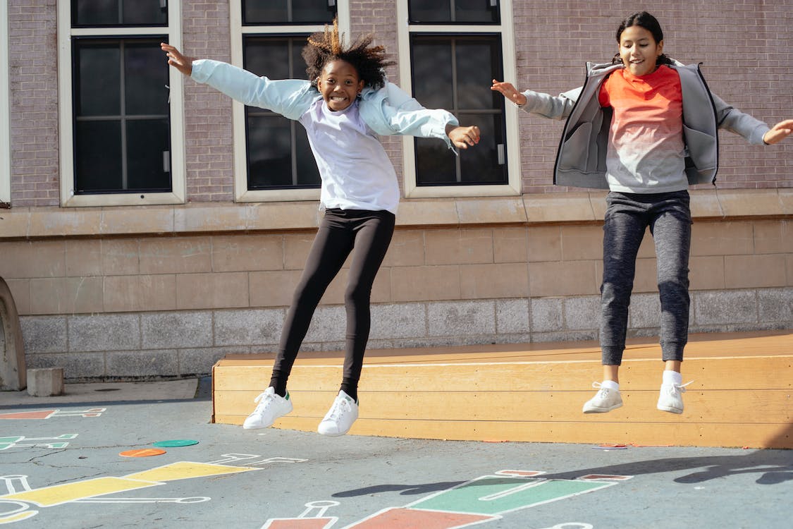 Two girls jumping off a box during recess on a school playground