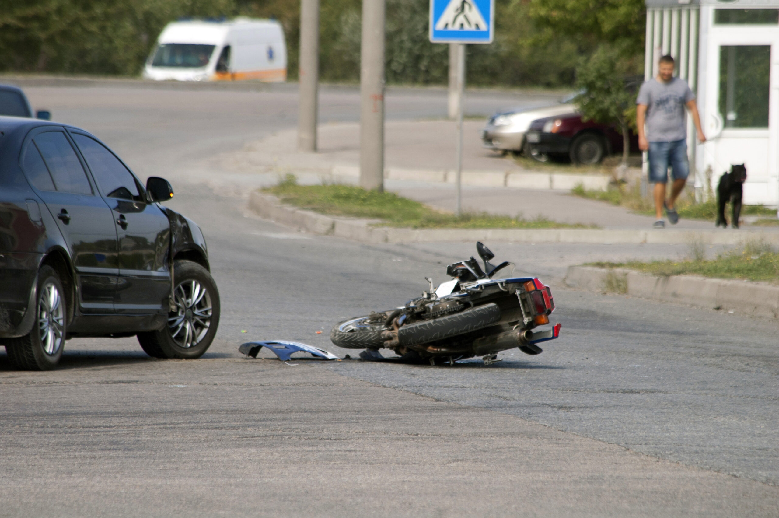 Scene after a motorcycle and black car crashed. Man walking his dog in the distance