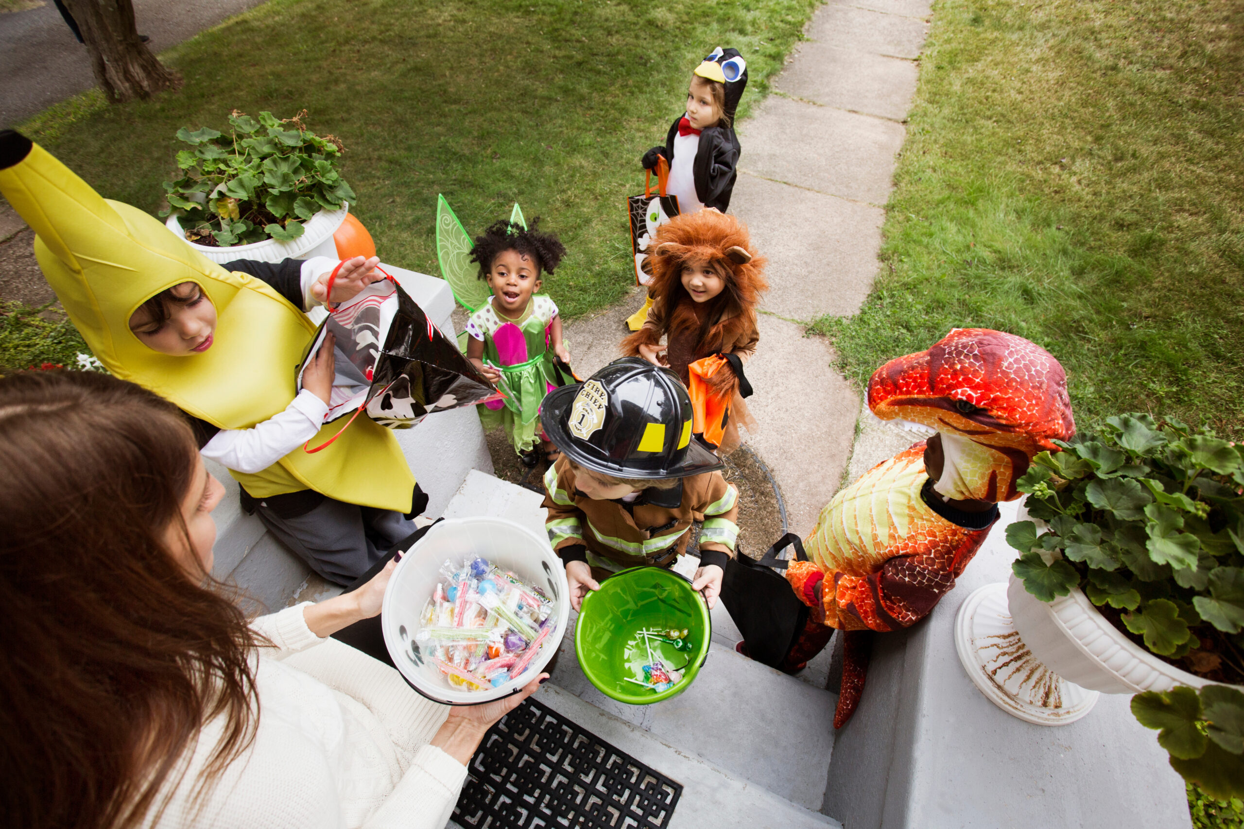 Young children, dressed in Halloween costumes, are trick or treating at a woman’s front door