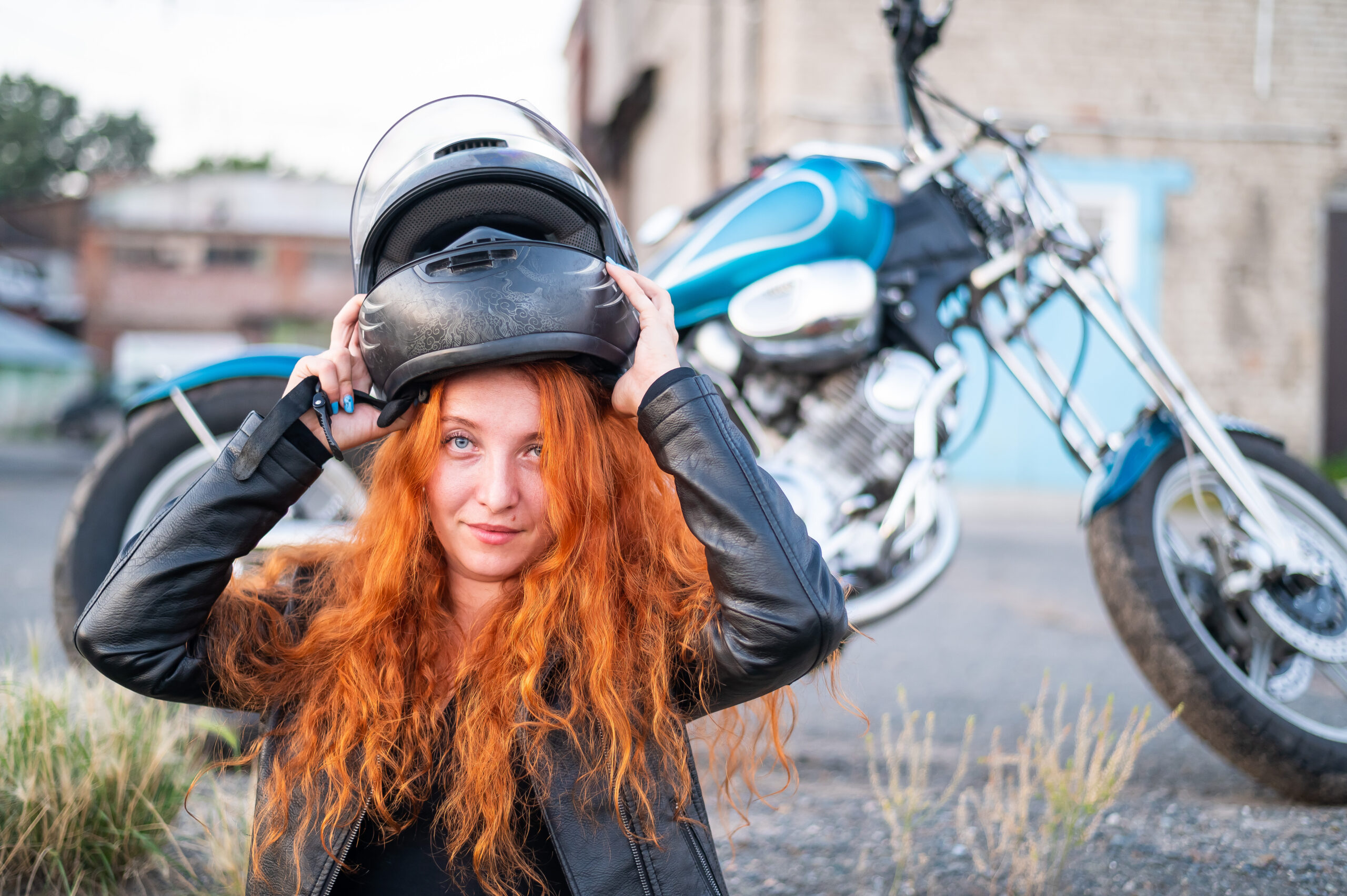 A red-haired woman puts on a helmet for safe motorcycle riding