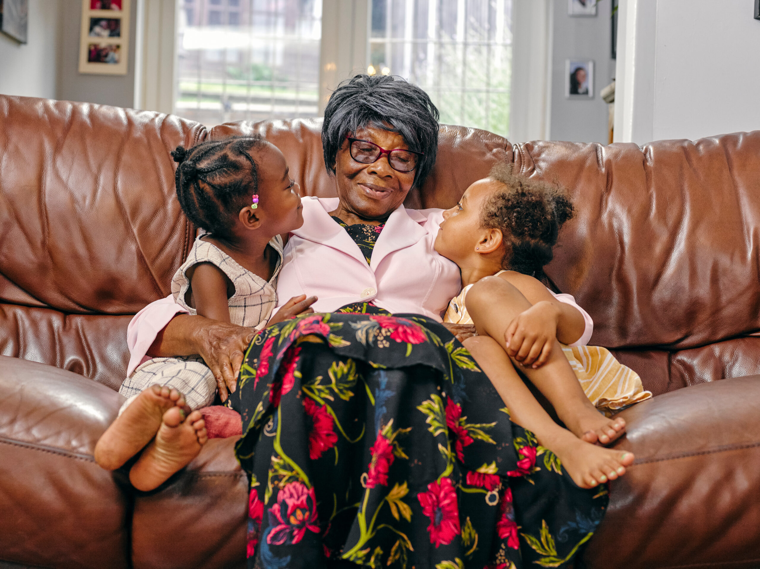Centenarian Great grandmother sitting on sofa with great granddaughters