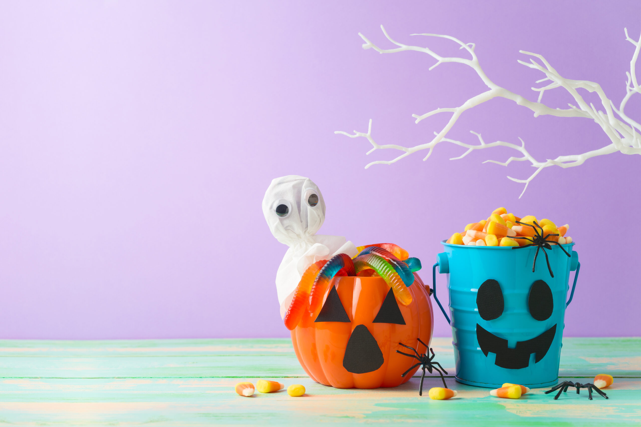 Halloween candy in orange and teal buckets on a purple background