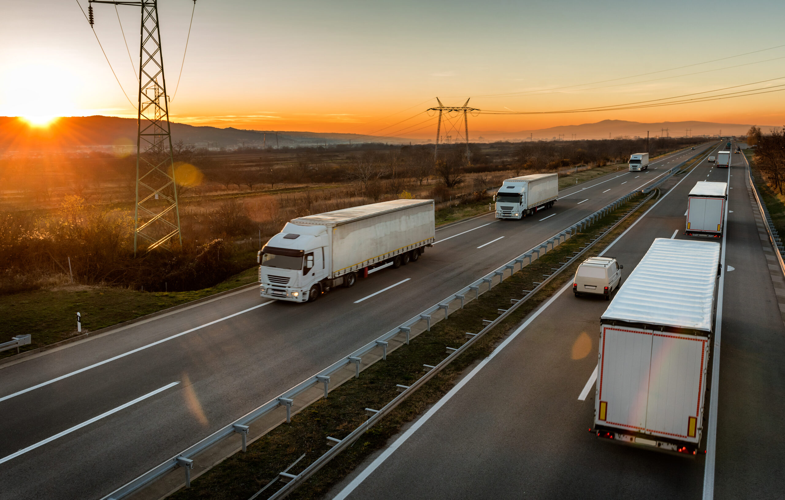 Convoys of White semi-trucks passing each other on a highway with a sunset and mountains in the background